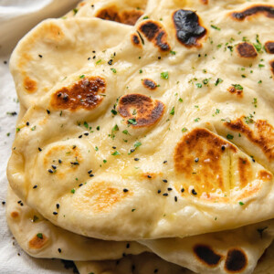 Close up shot of homemade naans stacked on top of each other and topped with garlic butter