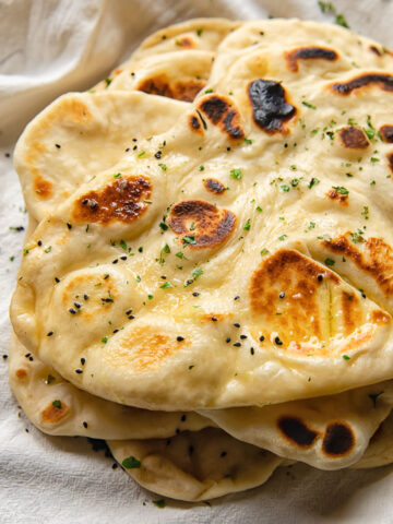 Close up shot of homemade naans stacked on top of each other and topped with garlic butter