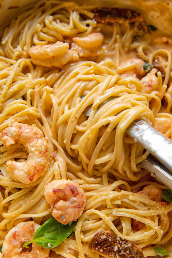Close up shot of marry me shrimp pasta being served with tongs from a pan