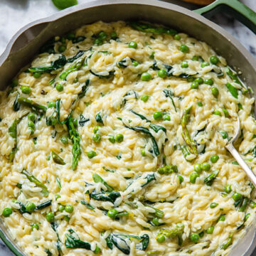 Top down view of creamy orzo pasta with peas and spinach in a pan