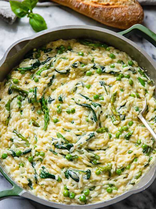 Top down view of creamy orzo pasta with peas and spinach in a pan