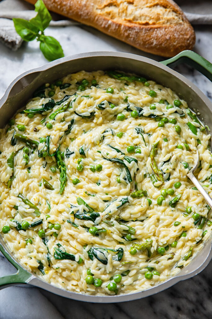 Top down view of creamy orzo pasta with peas and spinach in a pan