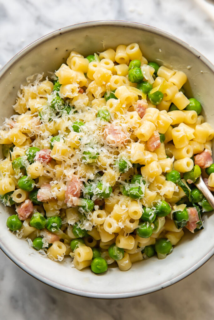Top down shot of pasta with peas in a bowl topped with grated Parmesan