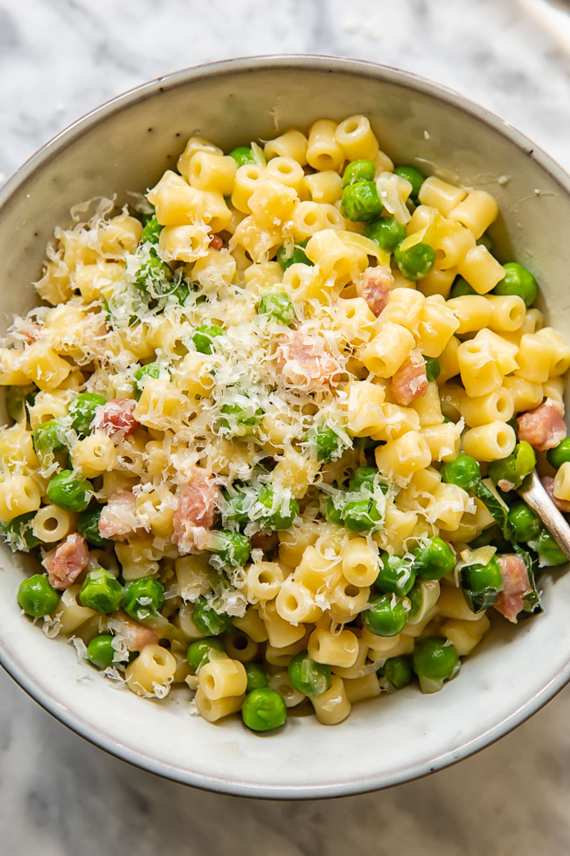 Top down shot of a bowl of pasta with peas, generously topped with grated Parmesan cheese.