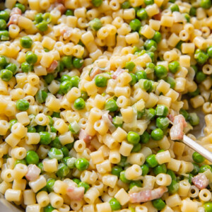 Close up shot of piselli pasta with peas and bacon bits in a large pan