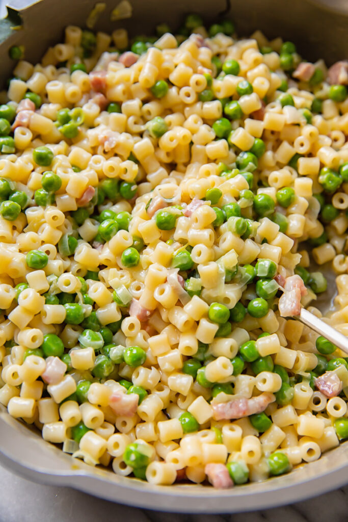 Top down shot of piselli pasta with peas and bacon bits in a large pan