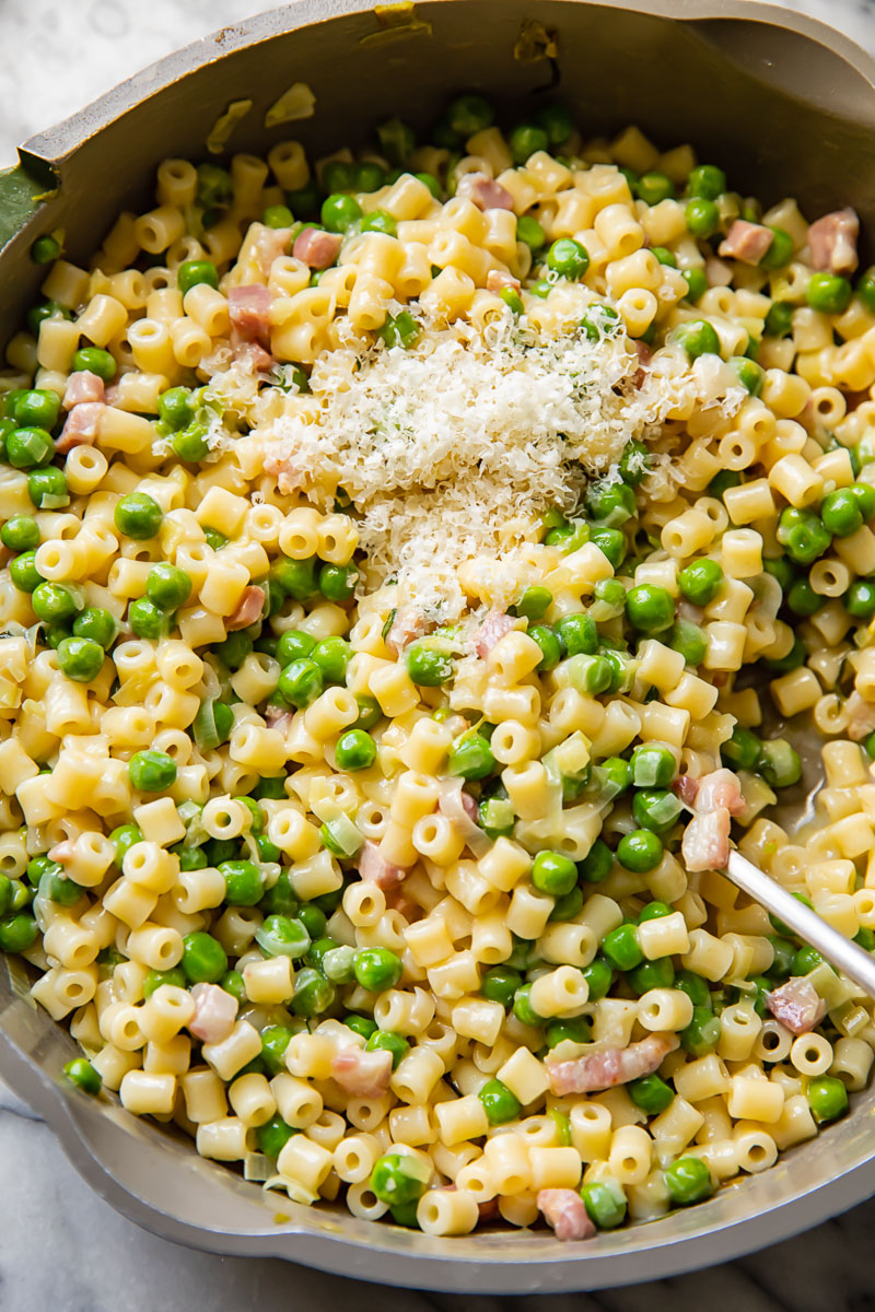 Top down shot of pasta e piselli with peas and Parmesan being scooped out of a large pan, showing its creamy texture.