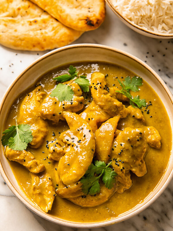 Top down shot of rich chicken and mango curry in a bowl topped with fresh cilantro