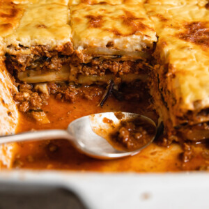 Close up shot of moussaka layers of beef and eggplant topped with creamy bechamel sauce along with a spoon