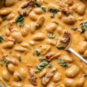 Top down shot of Tuscan butter beans in creamy sun dried tomato sauce in a pan with spinach