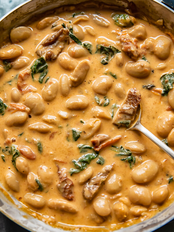 Top down shot of Tuscan butter beans in creamy sun dried tomato sauce in a pan with spinach