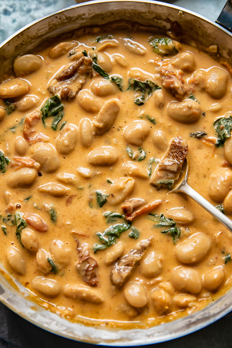 Top down shot of Tuscan butter beans in creamy sun dried tomato sauce in a pan with spinach