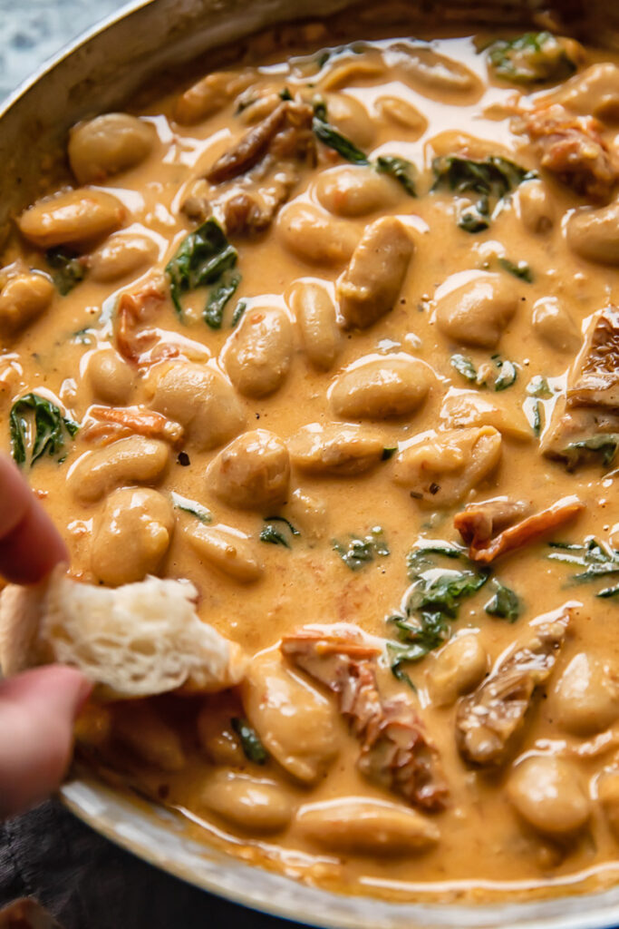 Close up shot of a piece of bread being dipped into tuscan butter beans sauce