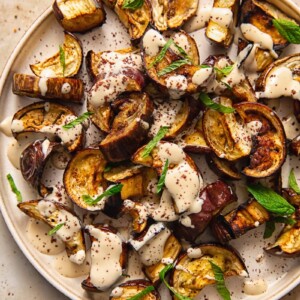 Close up of roasted aubergine on a plate with sauce and mint