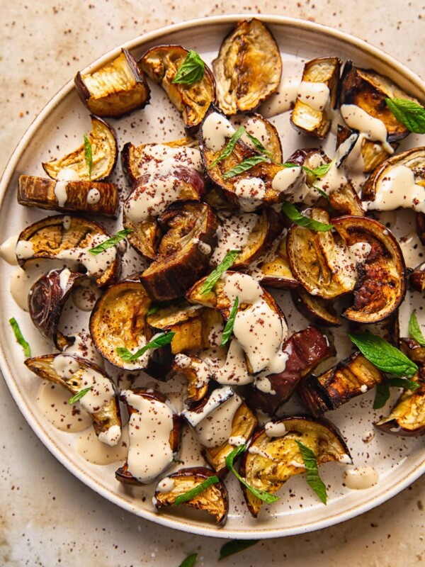 Close up of roasted aubergine on a plate with sauce and mint