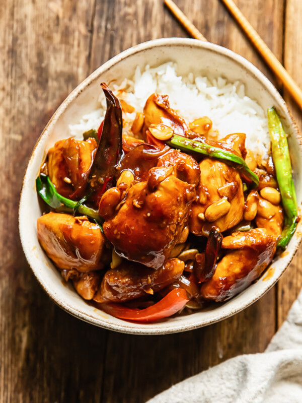 Top down shot of szechuan chicken with green onions and peppers on a bed of rice in a small bowl
