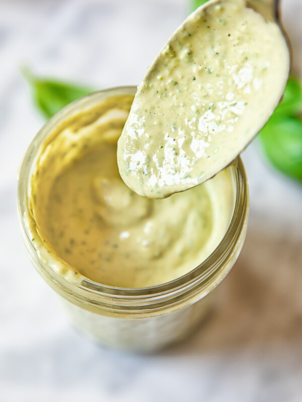 Close up shot of spoon serving tahini green goddess dressing into a glass jar