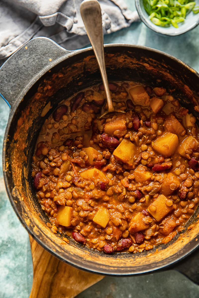 A top-down view of a steaming bowl of vegetarian lentil and butternut squash chili, adorned with fresh toppings.