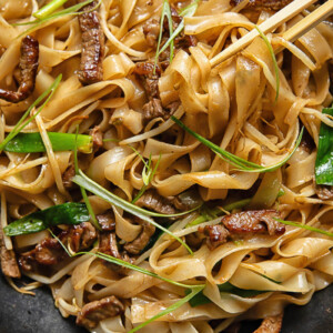 Top down shot of chop sticks picking up chow fun noodles with beef and beansprouts from a pan
