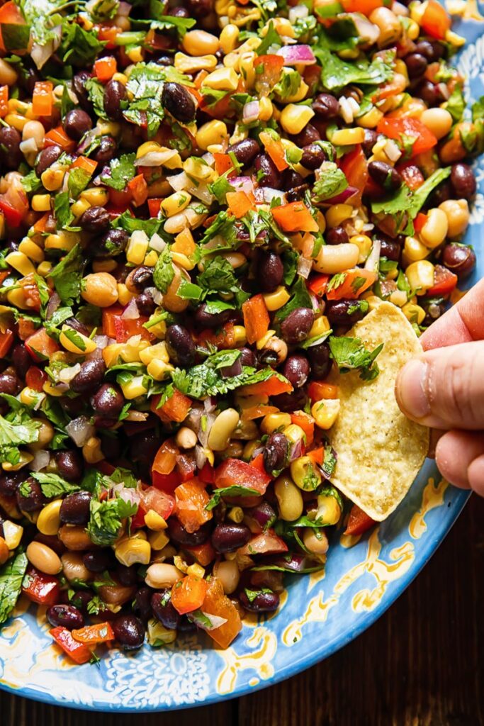 Close up shot of someone scooping up cowboy caviar salad with a corn tortilla chip