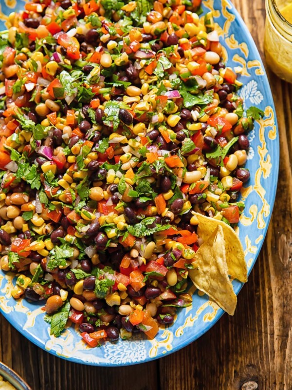 Top down shot of cowboy caviar on a large serving dish with beans, corn, pepper and tomatoes topped with dressing and fresh herbs