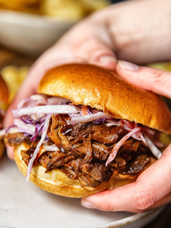 Close up shot of someone holding a pulled pork sandwich with fresh slaw