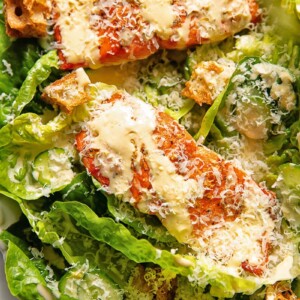 Close up shot of salmon fillets on a bed of lettuce with croutons, topped with Caesar dressing
