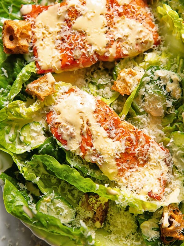 Close up shot of salmon fillets on a bed of lettuce with croutons, topped with Caesar dressing