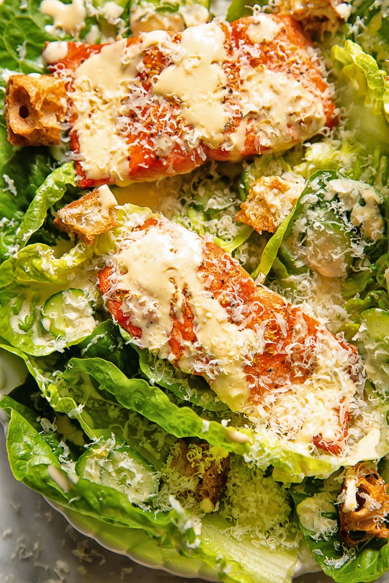 Close up shot of salmon fillets on a bed of lettuce with croutons, topped with Caesar dressing