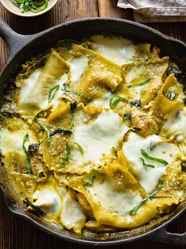 Top down shot of white chicken skillet lasagna in a pan topped with melted cheese and fresh basil