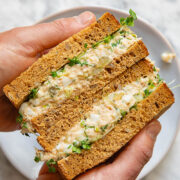Top down shot of person holding sandwich with tuna, egg and green onions cut in two halves
