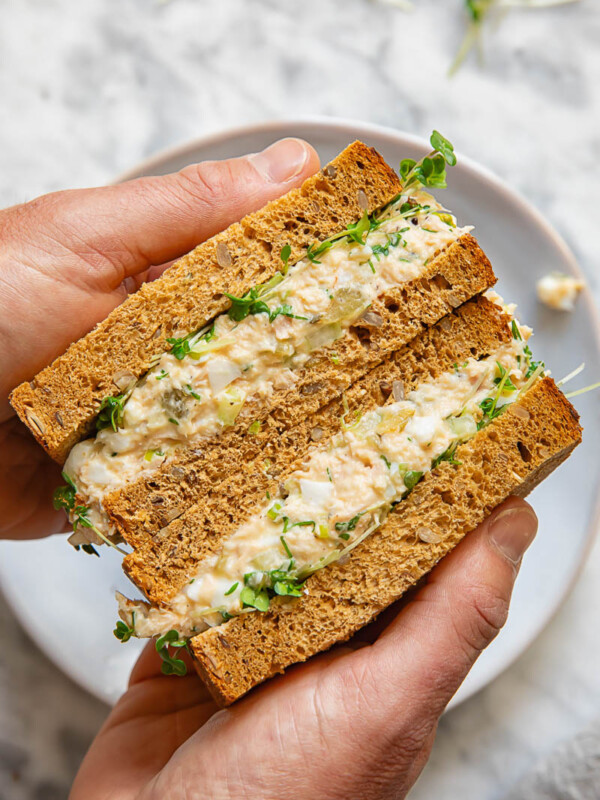 Top down shot of person holding sandwich with tuna, egg and green onions cut in two halves