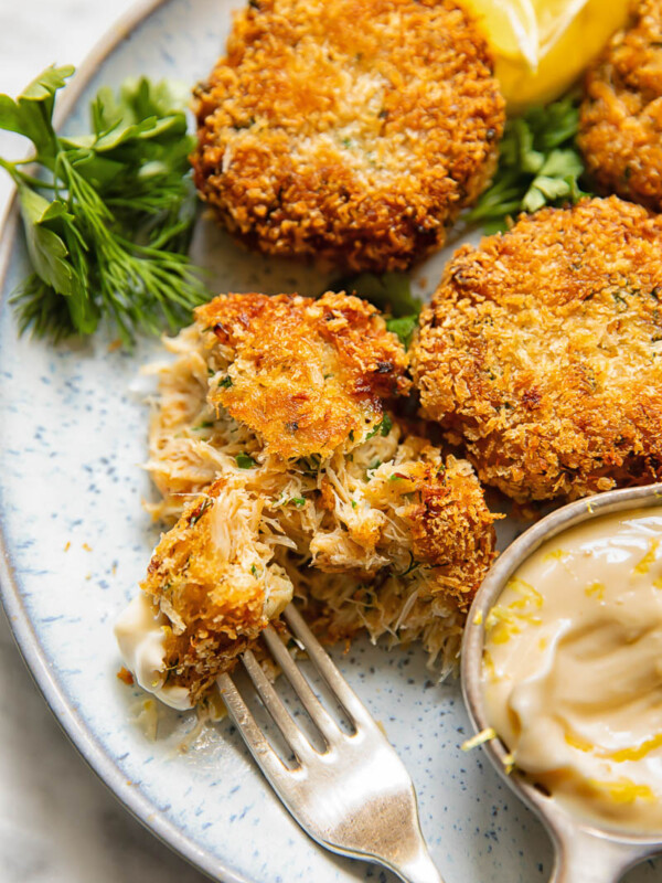 Close up shot of someone taking a bite of crab cake from a small plate