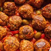 Top down shot of pork and beef meatballs in a pot with tomato sauce topped with olives and red pepper slices