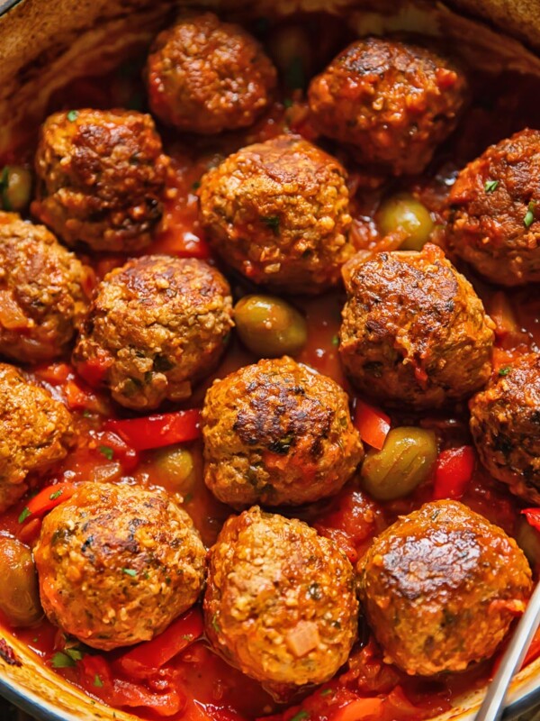 Top down shot of pork and beef meatballs in a pot with tomato sauce topped with olives and red pepper slices