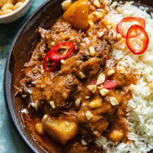 Close up shot of short rib massaman curry in a plate on a bed of rice topped with peanuts and chilli slices