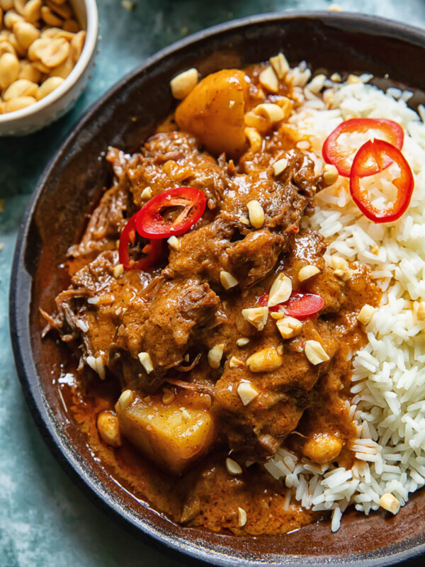 Close up shot of short rib massaman curry in a plate on a bed of rice topped with peanuts and chilli slices