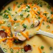 Top down shot of kielbasa soup in smooth potato blended broth being scooped out of a large pot