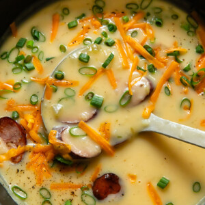 Top down shot of kielbasa soup in smooth potato blended broth being scooped out of a large pot