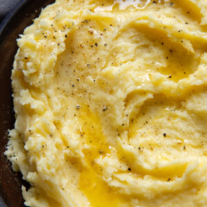Top down shot of mashed potatoes swirled on a small plate topped with grated Parmesan and black pepper