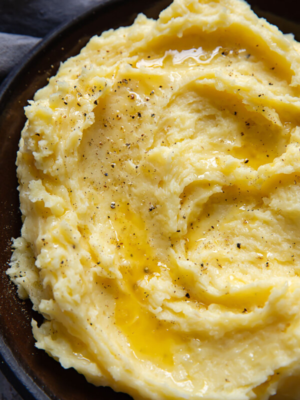 Top down shot of mashed potatoes swirled on a small plate topped with grated Parmesan and black pepper