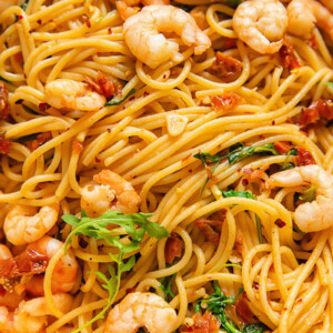Close up shot of shrimp and spaghetti with sun dried tomato and chilli sauce topped with arugula