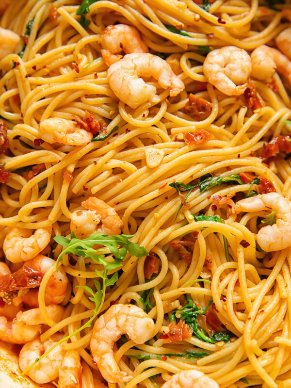 Close up shot of shrimp and spaghetti with sun dried tomato and chilli sauce topped with arugula