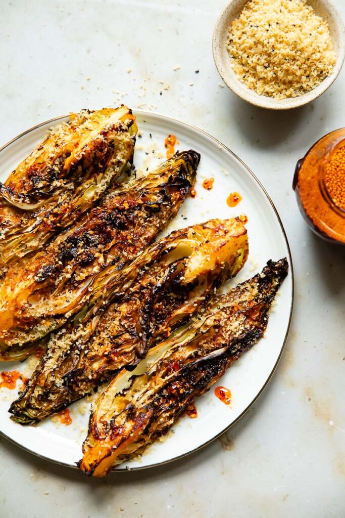 Gochujang roasted cabbage on a plate next to a bowl of breadcrumbs