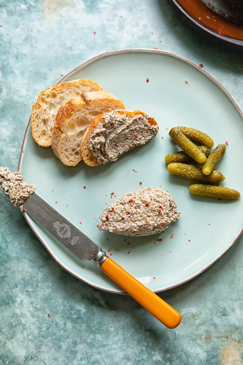 Shot of artisanal bread slices on a wooden board with mushroom paté spread generously on top, garnished with fresh herbs.