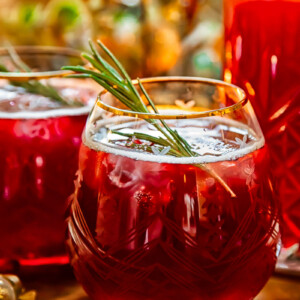 Side shot of pomegranate christmas punch in a glass with rosemary garnish