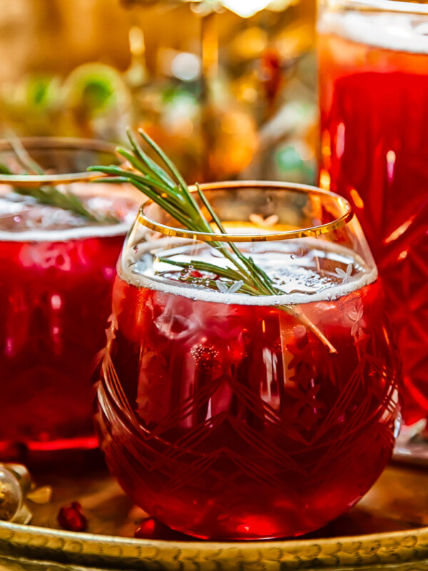 Side shot of pomegranate christmas punch in a glass with rosemary garnish