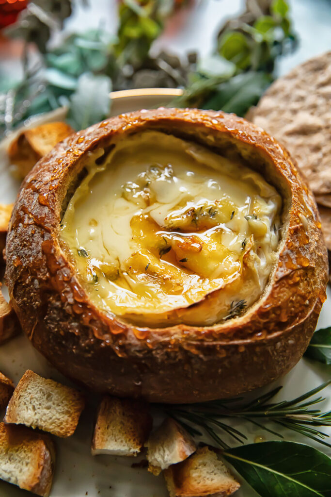 baked camembert in a bread bowl next to toasted bread slices