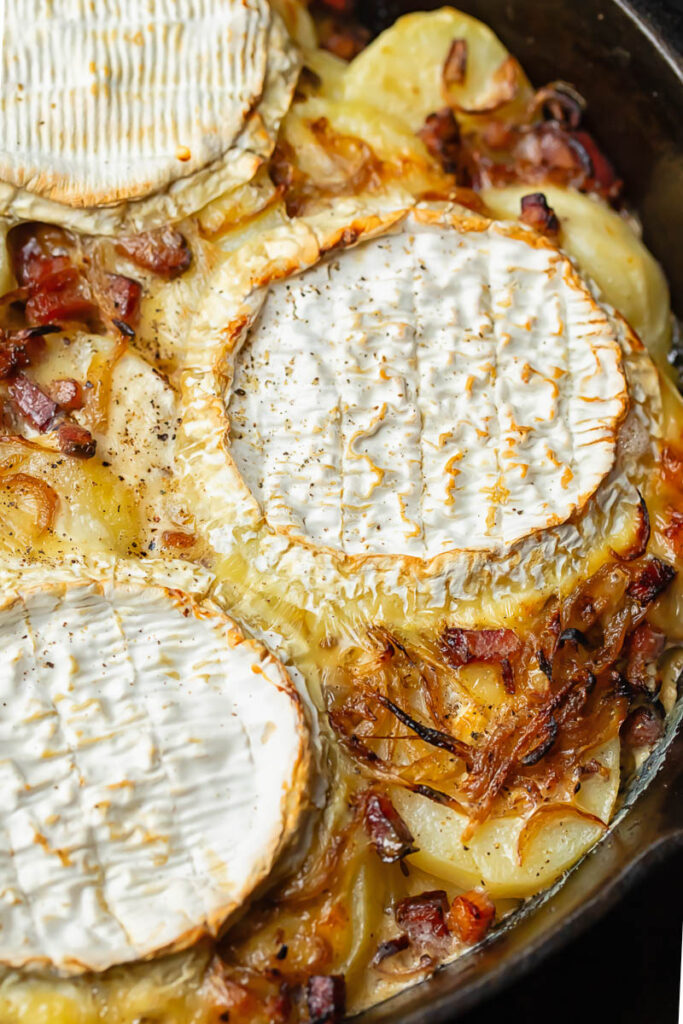 Close up shot of tartiflette in a pan with camembert wheels