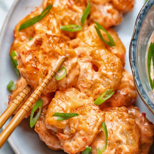 Close up shot of bang bang shrimp being picked up from a plate with chop sticks